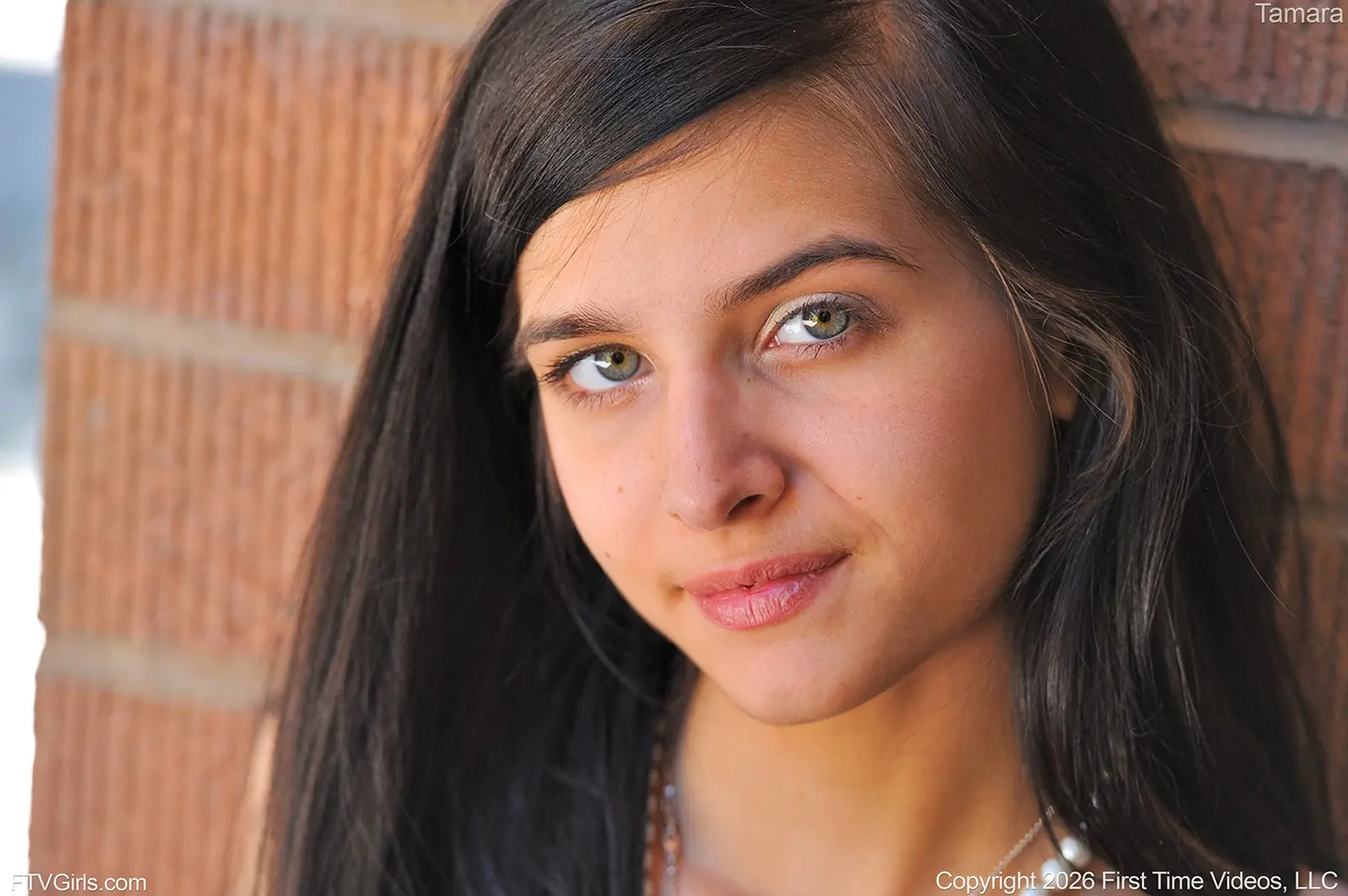tamara-ftvgirls-close-up-green-eyes-brick-wall Close-up portrait of Tamara with long dark hair and light green eyes against a red-brick wall